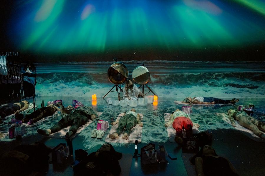 Sound healer between two gongs as guests rest on mats under the projected aurora