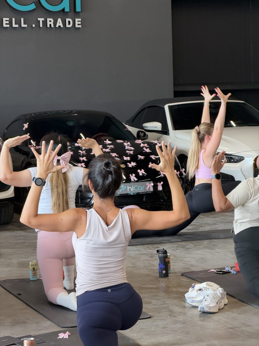 Guests in a kneeling lunge with arms raised in front of supercars at the hiCar showroom